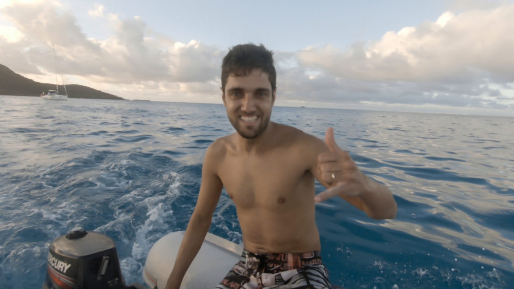 Pedro making a shaka driving the dinghy boat. Crystal waters surrounding it.