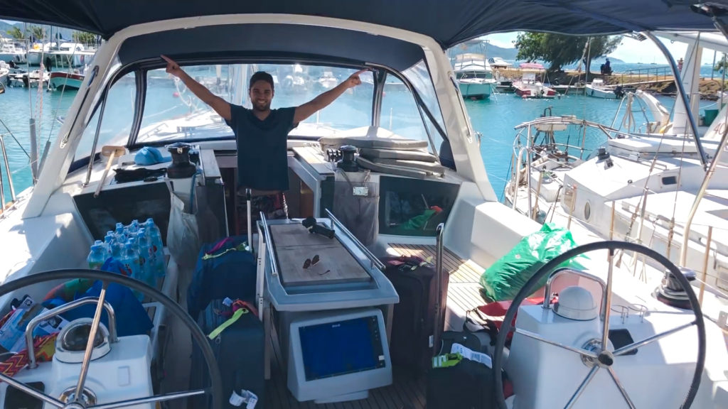 Pedro lifting arms in the sailboat's cockpit and several provisioning boxes laying around