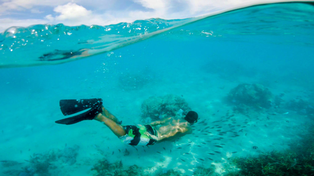 Pedro snorkeling next to Motu Vaiorea wearing fins and a green shorts.