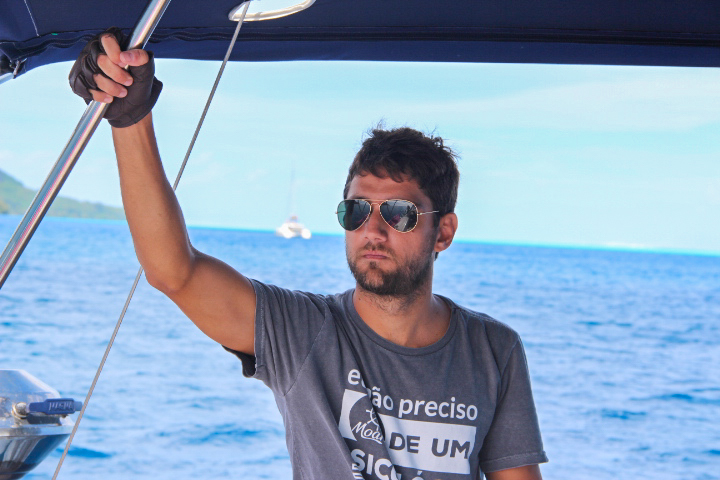 Pedro on the boat holding the rigging and wearing gloves and rayon-like sunglasses